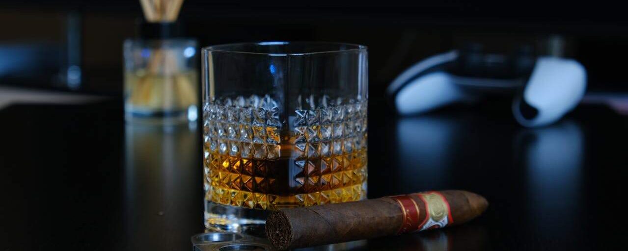 A glass of whisky with a cigar on a dark tabletop, embodying luxury and relaxation.